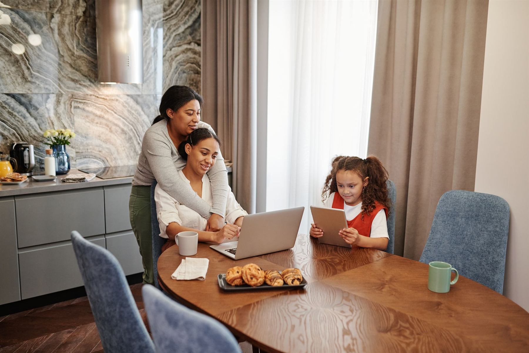 A family sitting together at a kitchen table with a laptop and a tablet